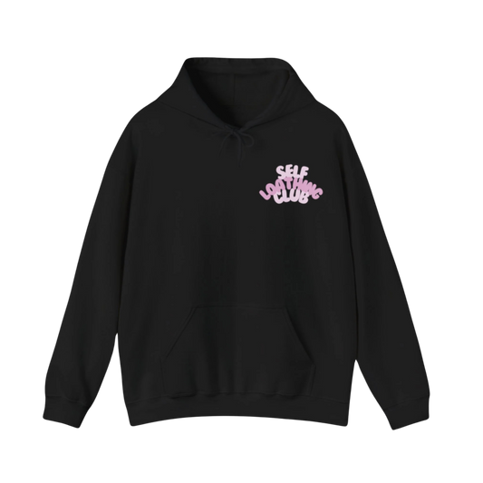 Black hoodie with front pocket and drawstring, featuring pink “SELF LOATHING CLUB” text in rounded font on upper left chest
